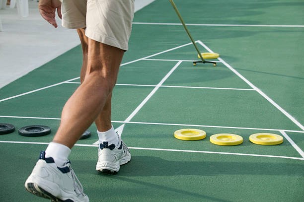 Court shuffleboard player completing a shot with the cue kept low on the court.